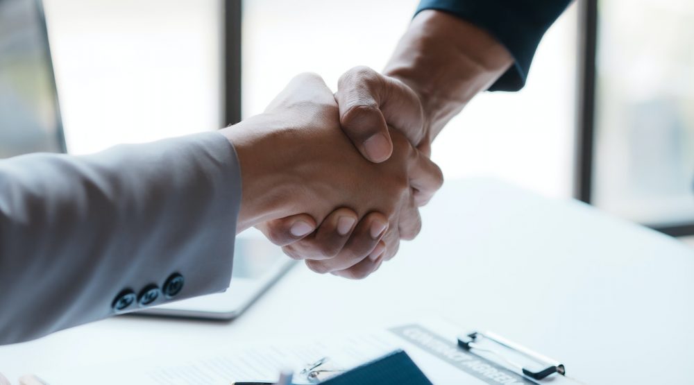 Real estate agent shakes hands with a client to sign a home purchase contract congratulating
